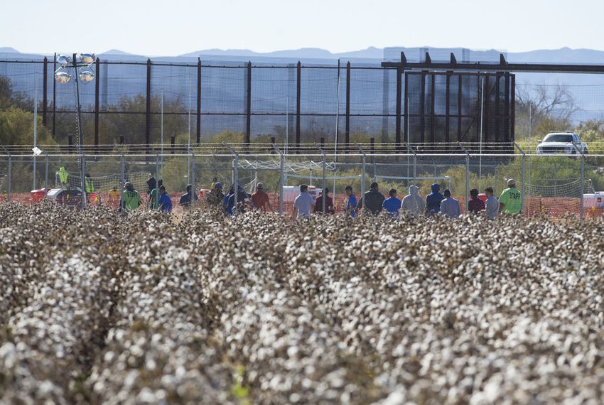 With cotton fields in the foreground and the border fence in the back, young boys walk with staff inside the tent city in Tornillo on Thursday, Nov. 15, 2018.