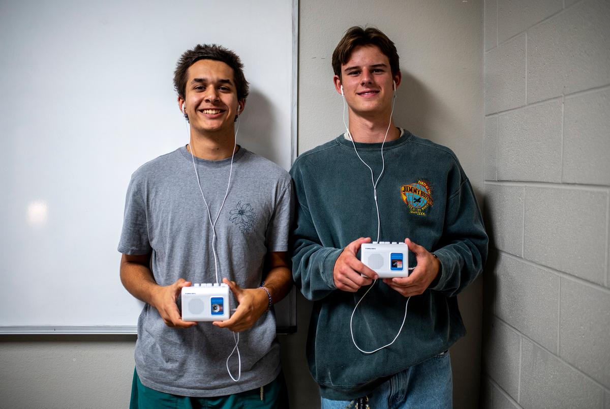 Seniors Jonah Farrington and Tripp Henderson display their cassette tape players at Lago Vista High School on Tuesday, Sept. 9, 2025 in Lago Vista, TX. Following the passing of HB 1481 Lago Vista has implemented a policy where students stow devices, primarily cell phones, in magnetically locked pouches that also block cell phone service, the devices can be unlocked in the event of an emergency as well as when the students exit the building using a wall mounted key near the building entrance. Due to the new policy some students have begun bringing in music players like tape players or mp3 players to still be able to enjoy music while at school. (Sergio Flores for The Texas Tribune)