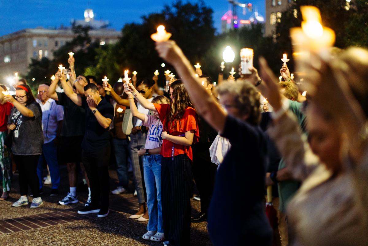 Candle flames light up the night as community members raise their hands in a moment of silence during a vigil at Travis Park in San Antonio on Monday, July 7, 2025. Organized by Centro San Antonio, the event honored the memory of more than 80 lives lost in the devastating floods that swept across Texas.