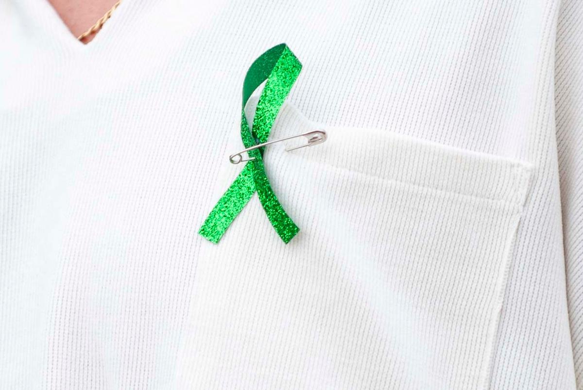 A green ribbon is seen on a shirt of an attendee during a Kerr County Blessing at Antler Stadium on Wendsday July 9, 2025 in Kerrville, Texas. The green ribbon repersents the flood victims of Camp Mystic.