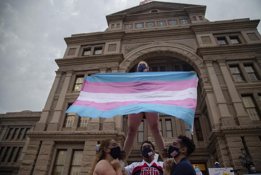 Ali Cross of the Austin Cheer squad waves a trans flag while her squad mates hold her up on the steps of the state Capitol at a rally against anti-trans legislation on April 28, 2021.