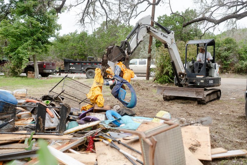 Sergio Galindo drives an excavator to move items to be discarded from a house cleanup after the flood in Hunt on Friday July 11, 2025.