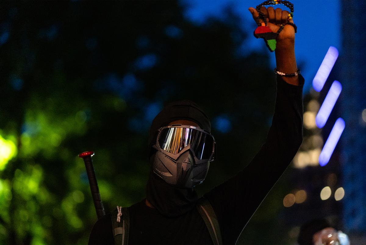 A protester armed with a baseball bat kneels in the street with fist upraised as protesters clashed with police in downtown Austin on Aug. 1, 2020.
