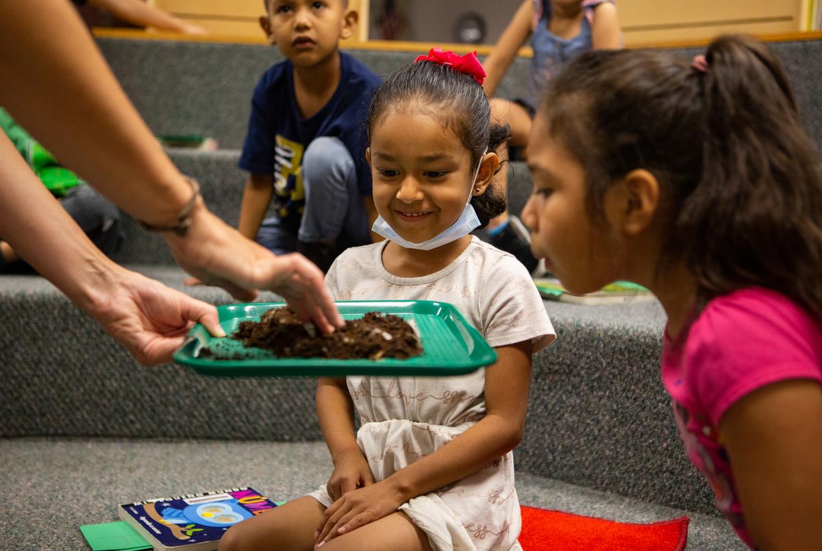 Students look at worms during a library lesson, which they have once per week, on Apr. 21, 2022. Cardenas always stays for the lessons to help keep them focused and translate when needed. The librarian tries to coordinate lessons that fit the themes Cardenas is teaching. This lesson was about how worms are present in soil when it is rich. They wanted students to learn that 