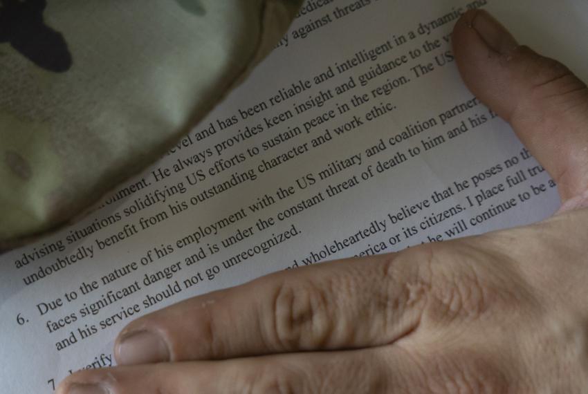 A letter, only part of which is visible because a hand and a piece of fabric obscure some of the text. The visible portion says the U.S. would “undoubtedly benefit from his outstanding character and work ethic.” It also says a person, whose name is obscured, “faces significant danger and is under constant threat of death” due to a someone’s work with the U.S. military.