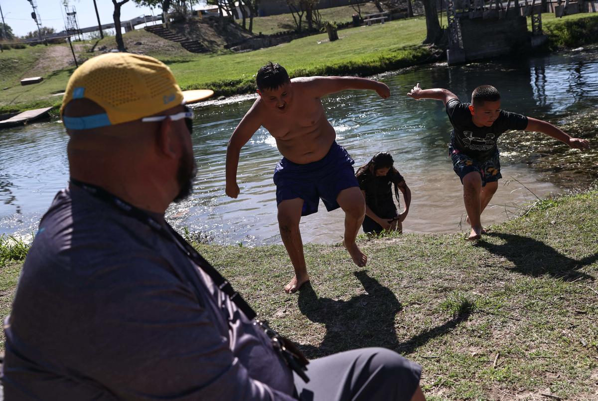 The Treviño siblings race to get back to shore after jumping from a suspension bridge into the water as their father, David, watches them at Blue Hole Park in Del Rio on March 25, 2023.