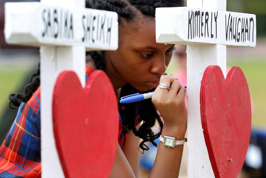 Jai Gillard, a freshman at Santa Fe High School, writes a message on a cross at a makeshift memorial left in memory of the victims killed in a shooting in Santa Fe, on May 21, 2018.