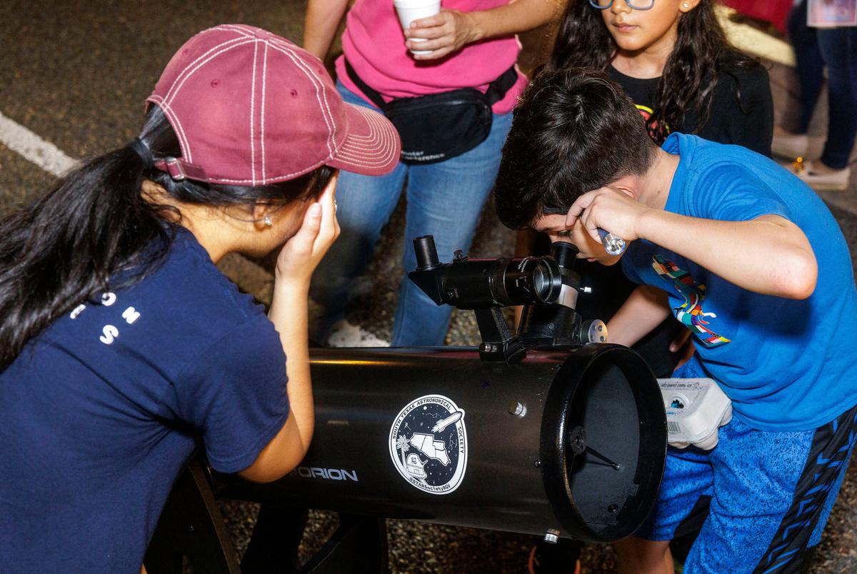 Staff members from the South Texas Astronomical Society  organization oversee a telescope setup for passersby to see stars at a night market in Brownsville on Sept. 20, 2025.