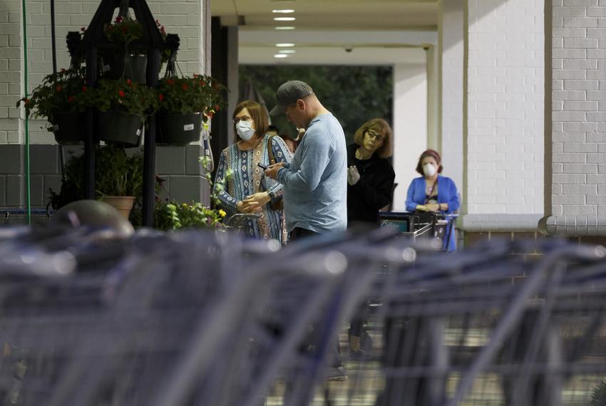 People with and without masks wait outside of a grocery store in Houston on March 31, 2020.