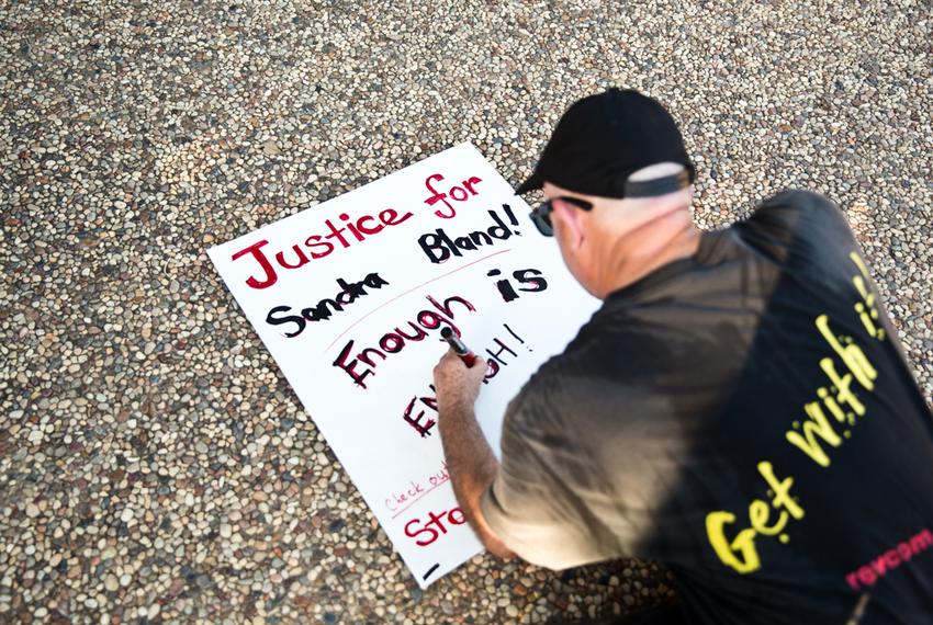 An attendee kneels to makes a sign during the vigil for Bland.