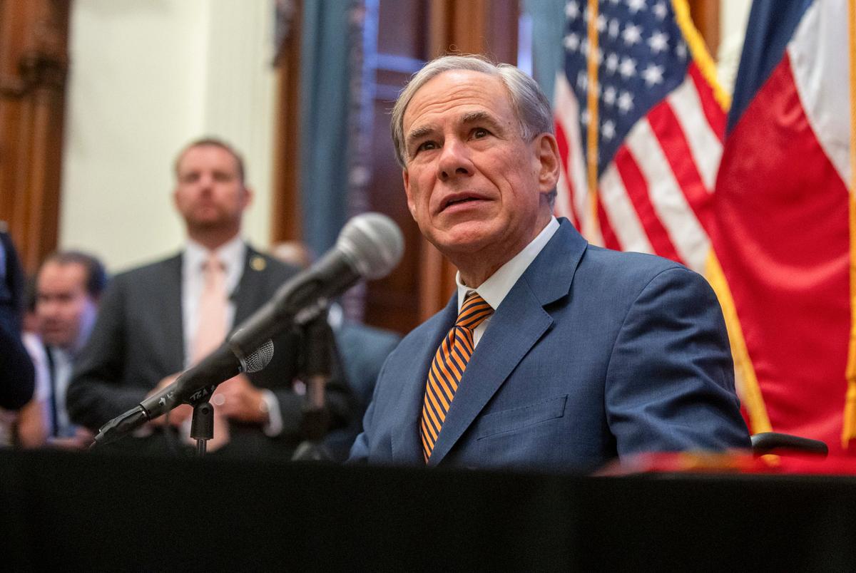 Gov. Greg Abbott speaks into a microphone with large Texas and U.S. flags behind him.