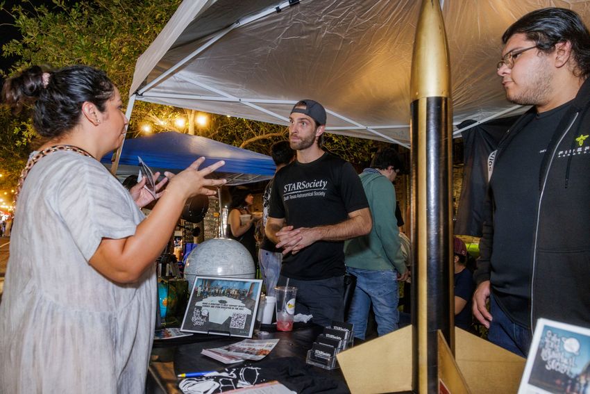 Blaine Allen, center, and Hector Salinas, staff members from the South Texas Astronomical Society organization, speak to a passerby at a night market in Brownsville on Sept. 20, 2025.