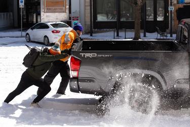 People push on the back of a truck to attempt to get the vehicle unstuck from the snow in Austin, Feb. 15, 2021.