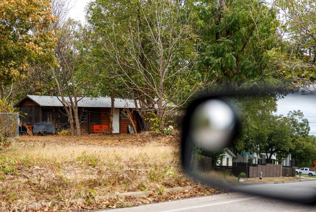 An older home in a single-family neighborhood displays a large orange sign reading "END CONSTRUCTION" on Sept. 16, 2023. Newly built duplex units at 4425 Jester Drive can be seen in the side mirror of a car in the foreground.