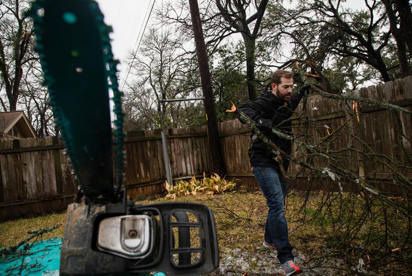 Aaron Nightingale clears away tree limbs from his backyard after an ice storm, in northwest Austin on Feb. 2, 2023. A large limb pierced through a portion of Nightingale's roof, but he was able to clear the rest with the help of Eric Calder and his son.