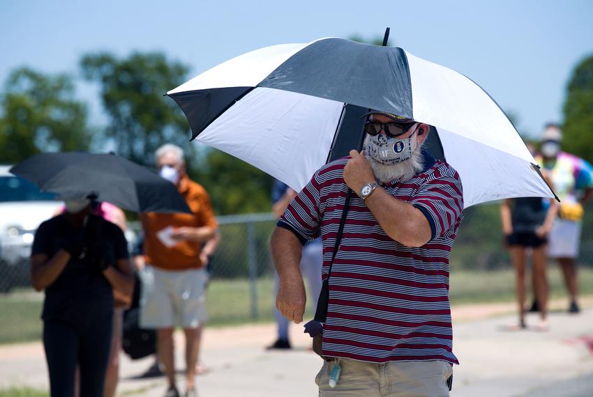 A voter uses an umbrella for protection from the sun. Voters waited in 100 degree temperatures outside the Pflugerville ISD Rock Gym  on Tuesday.