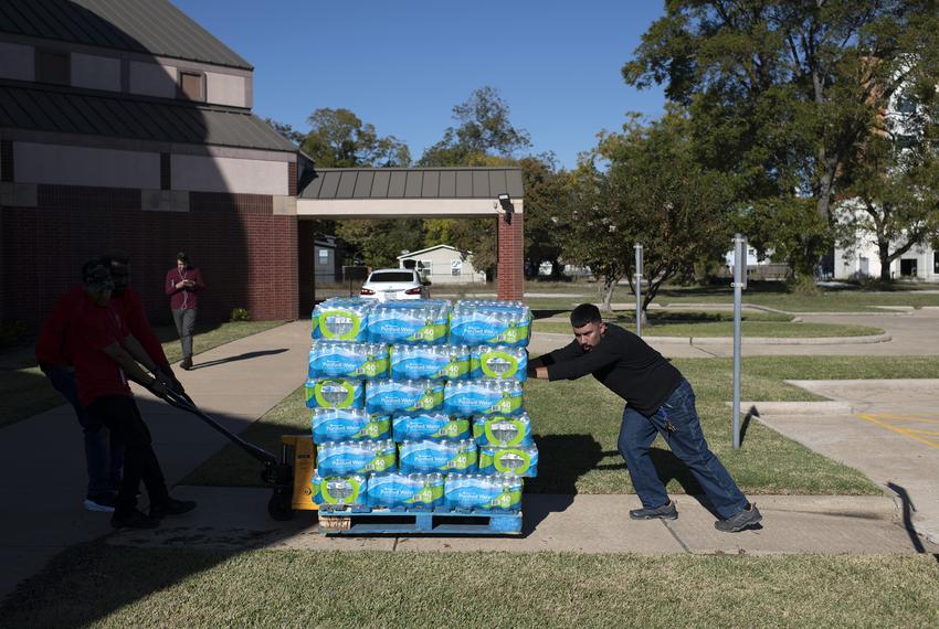 Isaiah Chirip helps push a pallet of bottled water during a water distribution and free flu vaccination event at the Holman Street Baptist Church in Houston on nov. 28, 2022.