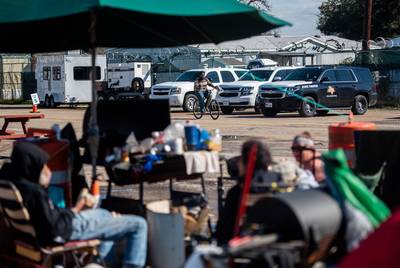 LaShawn Ramsey rides his bike infront of state emergency vehicles while Stephanie Baez's family has lunch at the state-sanctioned homelessness campsite in Austin on Jan. 23, 2020.
