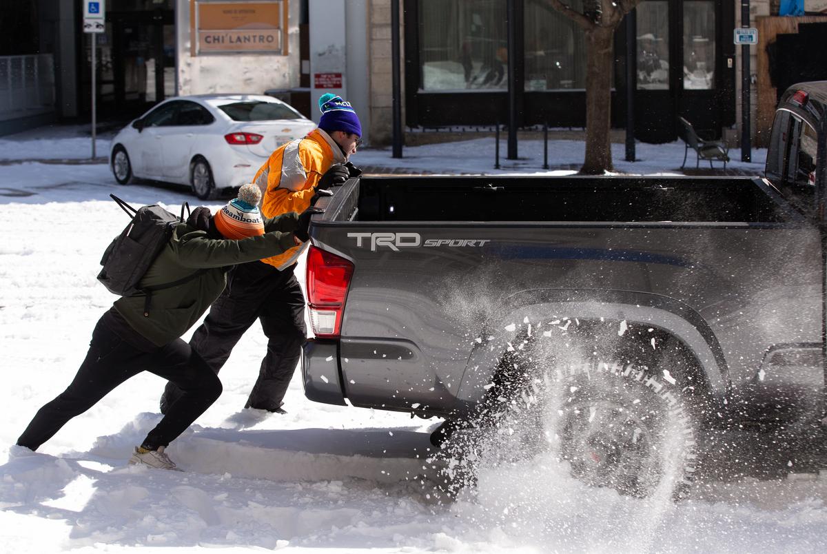 People push on the back of a truck to attempt to get the vehicle unstuck from the snow in Austin, Feb. 15, 2021.