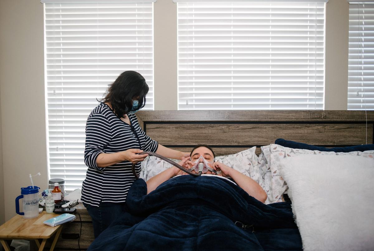 RICHMOND, MARCH 3:  Mauricio Marin's wife, Daysi, helps fasten his CPAP machine as he returns to bed at their home in Richmond, TX, on Wednesday, March 3, 2021.Mauricio Marin thought his worst days were behind him after his month-long stay in a Covid ICU late last year. Doctors sent the 44-year-old home to his wife and kids in Fort Bend County with oxygen tanks, a CPAP machine and strict instructions to avoid cold weather and the flu. But after four days mostly without power, no heat and inadequate oxygen that left him gasping for air, he told his wife, 
