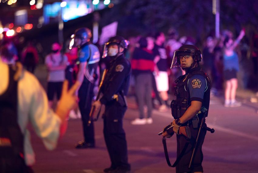 Austin police officers stand guard as the Austin Fire Department puts out a car that was set on fire by protesters in downtown Austin on May 30, 2020.