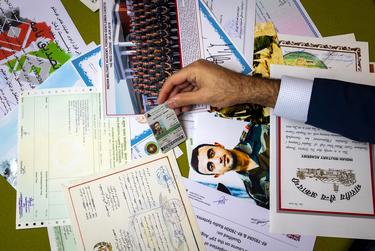 Sami-ullah Safi sorts through dozens of certificates and photos to pick up his brother’s ID card in his home in Houston on Sunday, Nov. 20, 2022.