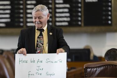 Rep. Charles “Doc” Anderson, R-Waco, holds a sign that reads, “Here we are still on the job for the people,” on the House floor on July 14, 2021.