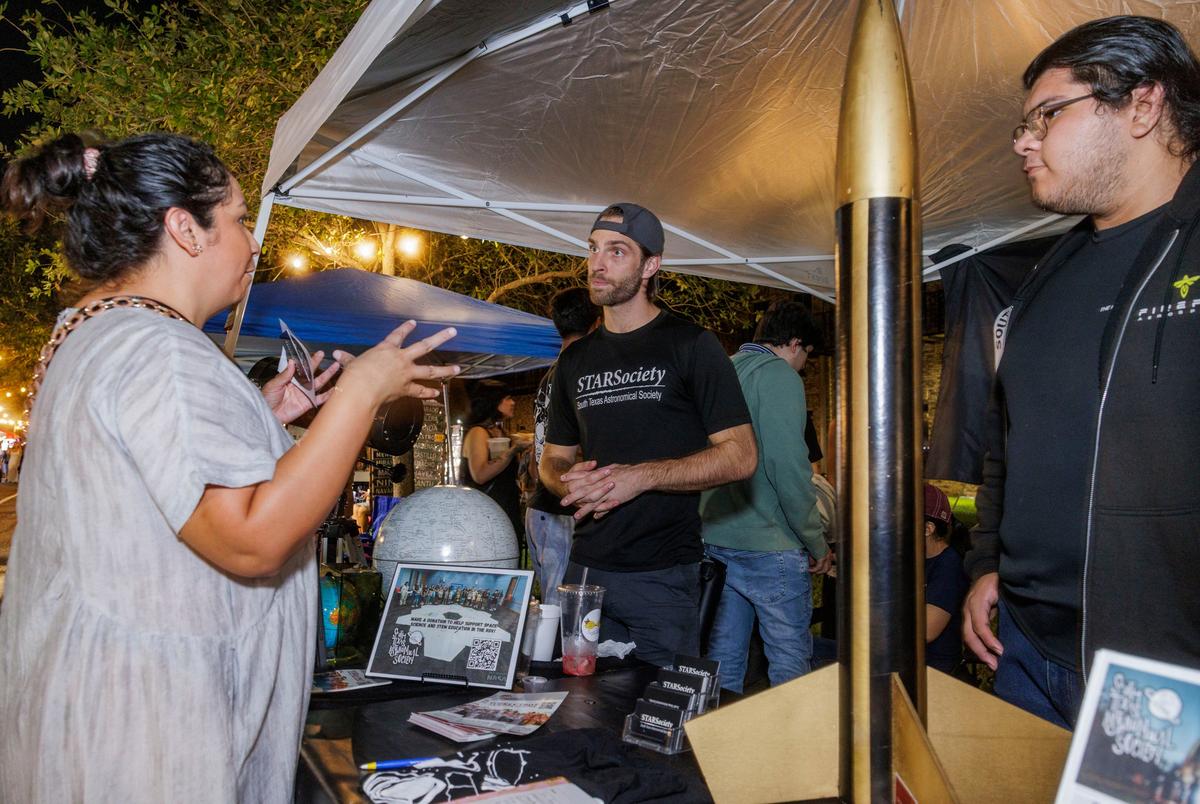 Blaine Allen, center, and Hector Salinas, staff members from the South Texas Astronomical Society organization, speak to a passerby at a night market in Brownsville on Sept. 20, 2025.
