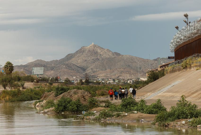 A group of migrants from Venezuela walk between the southern border wall and the Rio Grande river towards a temporary border patrol processing facility on October 6, 2022 in El Paso. Record numbers of migrants, mostly from Venezuela, began arriving at the US/Mexico border this month.