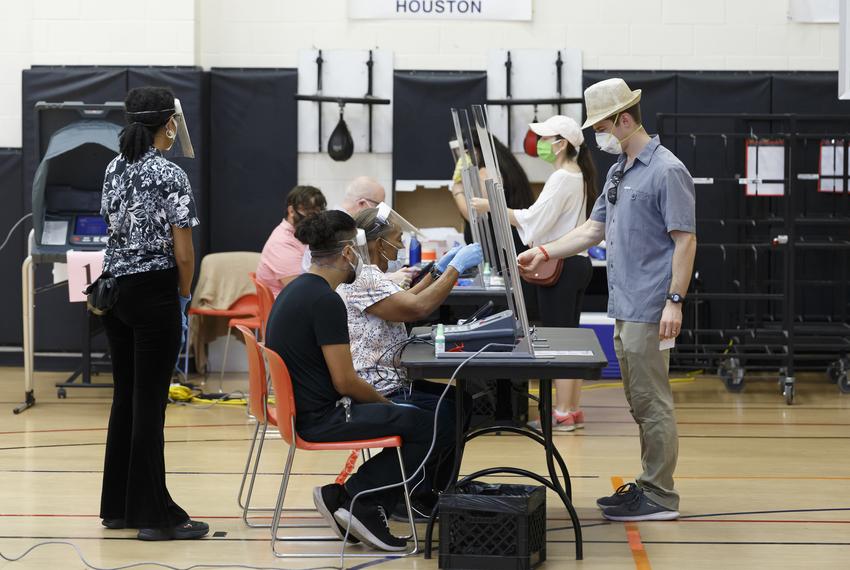 Voters check in with poll workers seated behind glass shields at the Metropolitan Multiservices Center in Houston for the delayed primary runoff election on Tuesday, July 14, 2020.