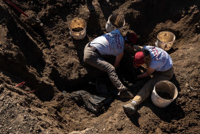 Isabel Melhado (left) and Olivia Messenger (right) remove dirt around the edges of a body bag containing the remains of an unidentified migrant buried at the Maverick County Cemetery in Eagle Pass on Jan. 10, 2023.