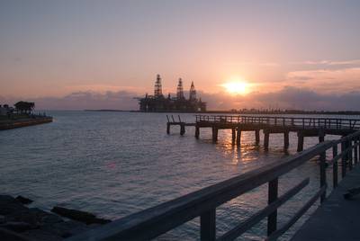 The sun sets on a fishing pier, damaged by Hurricane Harvey in 2017, in Port Aransas, Texas, on June 6, 2018. Three offshore oil rigs stand at attention in the distance.