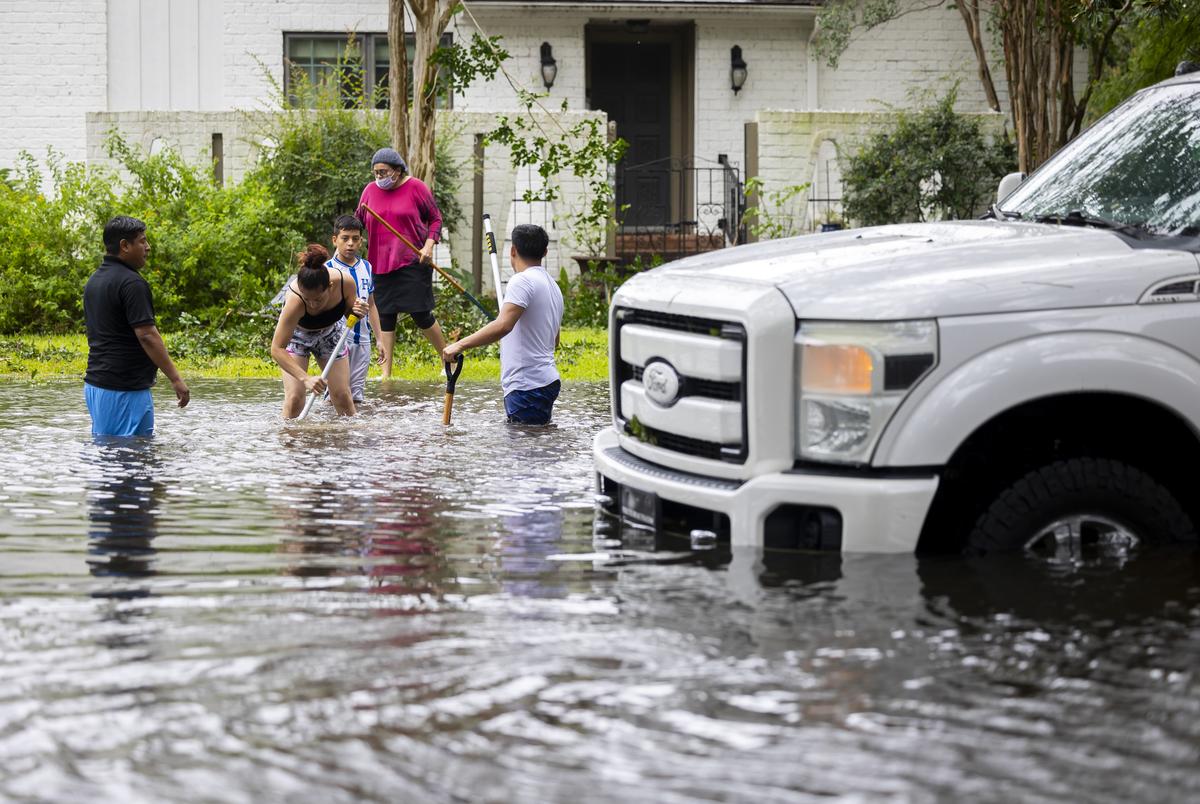 The Morales family works to unclog storm drains iacross the street from their house in Robindell during the aftermath of Hurricane Beryl on Monday, July 8, 2024, in Houston.
