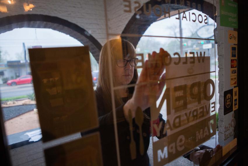 Brentwood Social House owner Suzanne Daniels tapes store hours and instructions on how to order on the store's front door. The coffee shop cut its hours of operation, closed its dine-in services and asked its customers to order and wait outside the coffee shop to comply with state and local ordinances. March 23, 2020. 