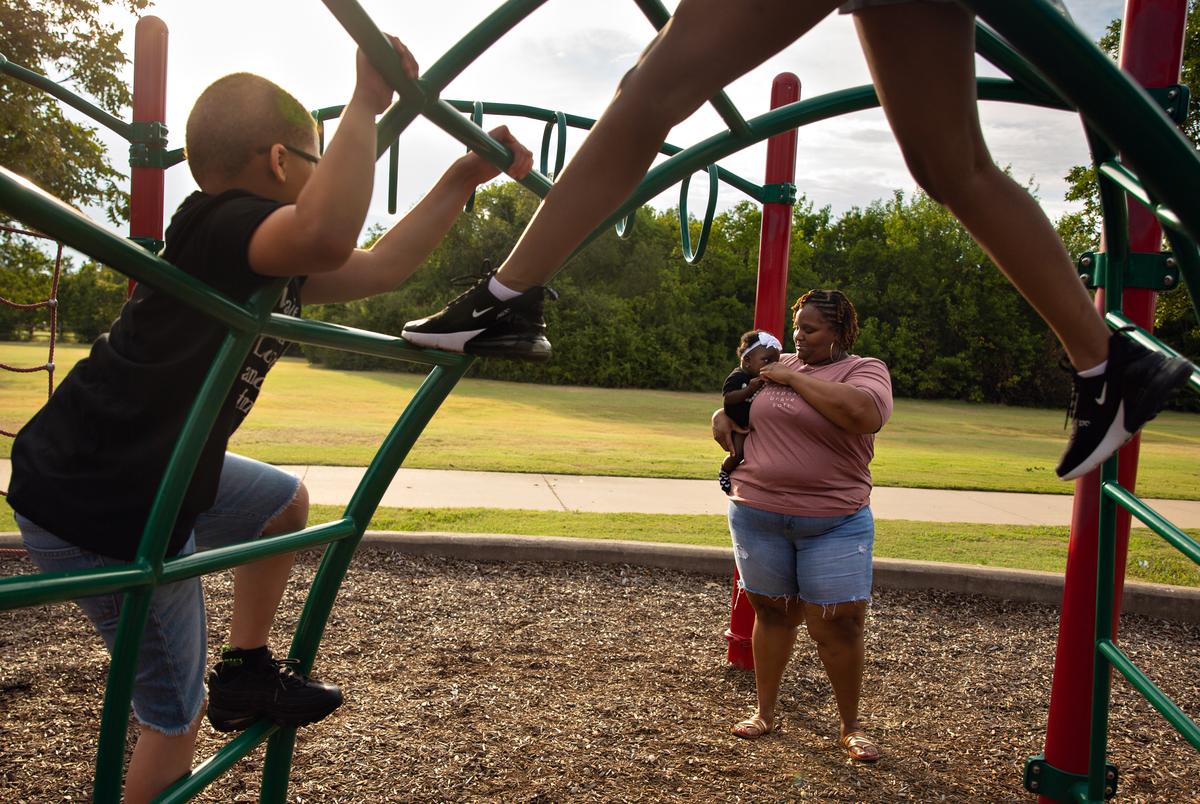 Tambra Morrison holds her 7-month-old daughter Kalani as they watch her other two children Kayden and Kynnedi climb the park jungle gym at Red Bird Park in Duncanville, TX on August 14, 2021.