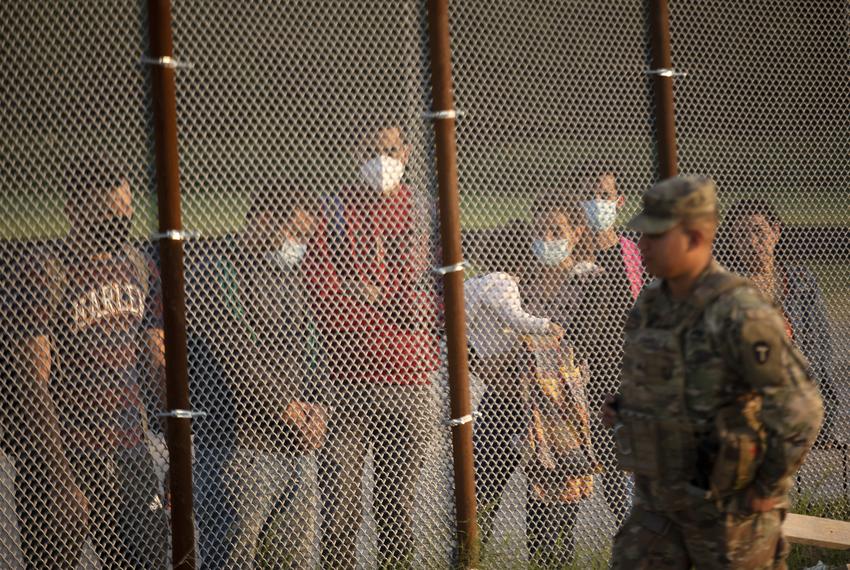 A National Guard soldier walks past a group of migrants. The group turned themselves over to Customs and Border Protection officials at the U.S. and Mexico border in Del Rio on July 22, 2021.