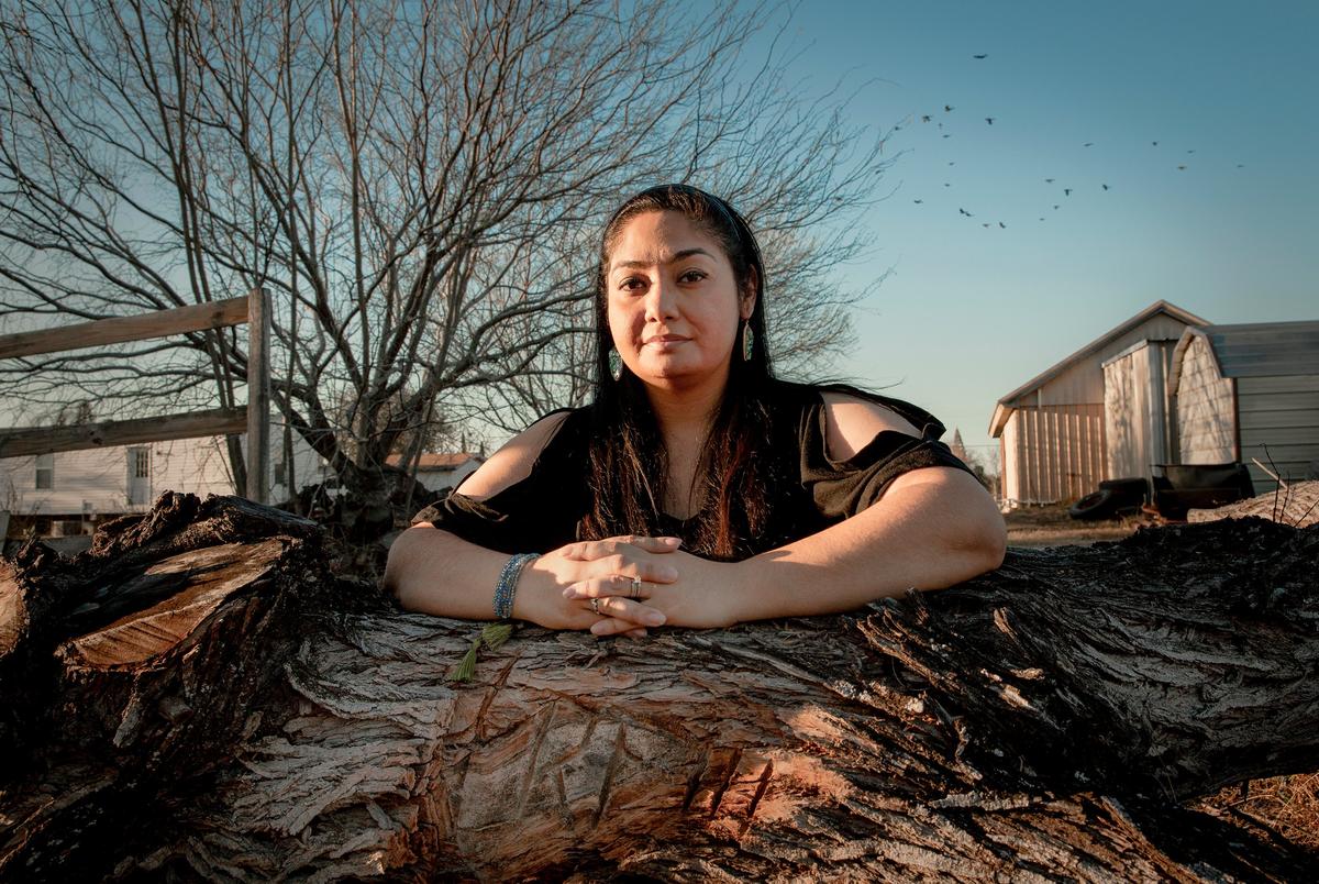 Beatrice Fuentes kneels on a mesquite tree with her husband's initials carved in the trunk. March, 5. 2021