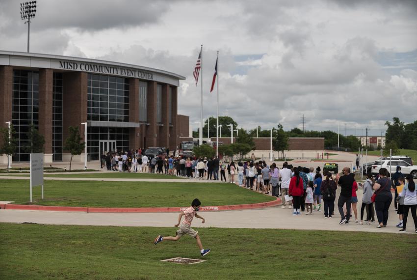 A young boy jumps over a drainage fence as McKinney ISD students and their legal guardians stand in a line to receive a COVID-19 vaccine at the McKinney ISD Stadium and Community Event Center on May 20, 2021.                                                                                                                                                                                                                                             